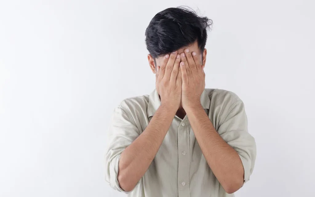 A man covering his face with hands, expressing feelings of stress and emotional struggle.